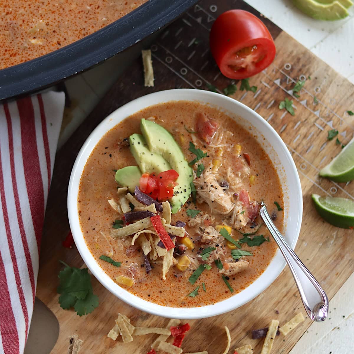 Chicken tortilla soup in a white bowl garnished with tomato, avocado, and tortilla chips.