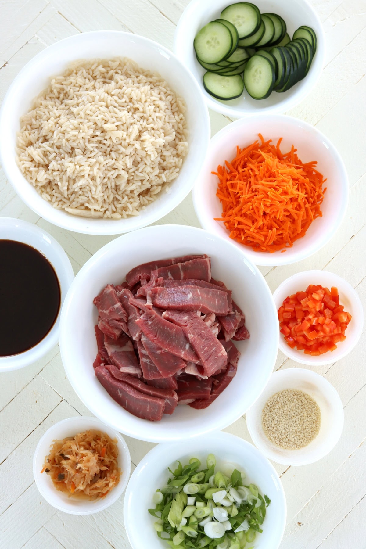 Ingredients needed for make Korean bbq bowls on a white wooden board.
