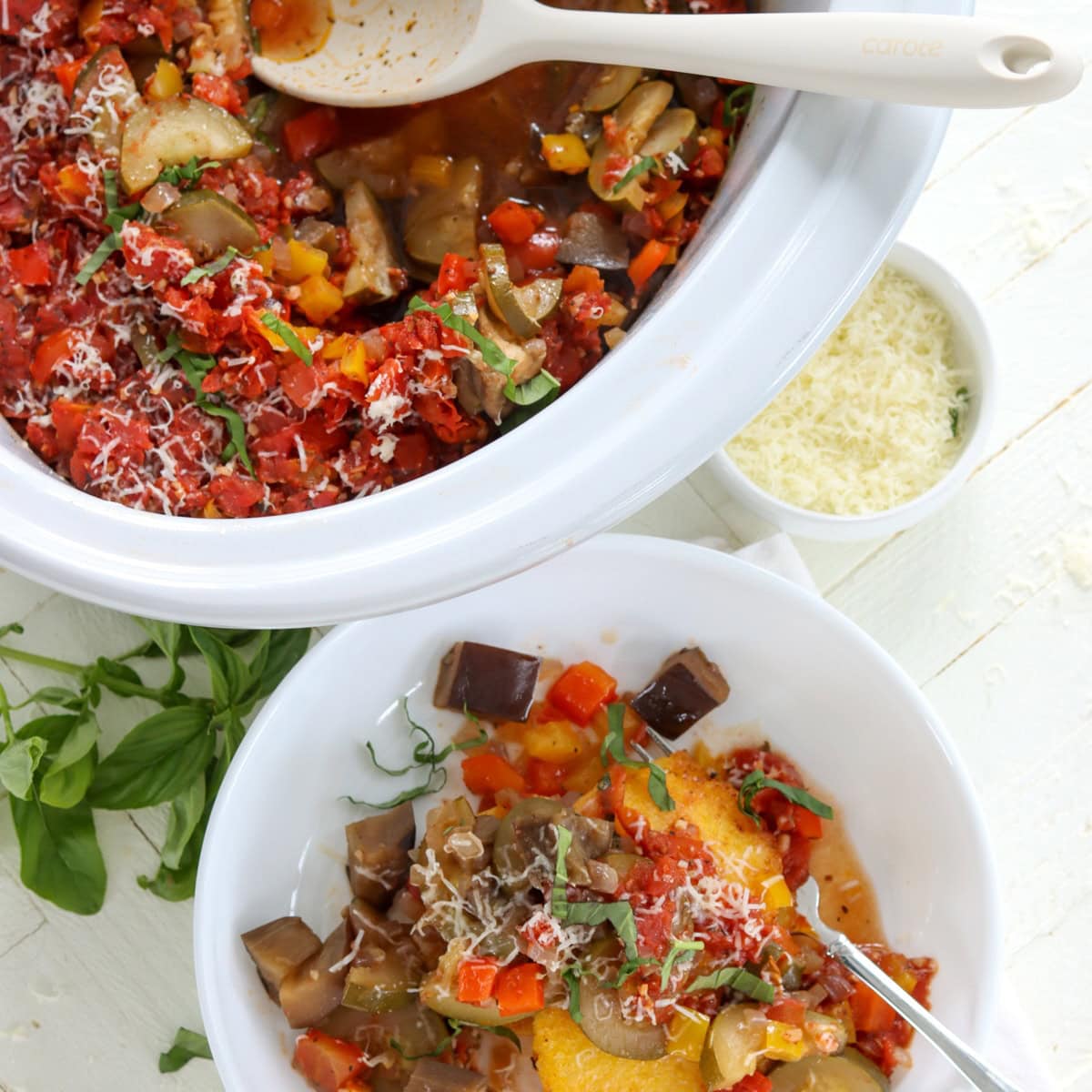 A white oval crockpot and white serving bowl of ratatouille slow cooker recipe.