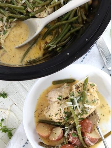 Chicken and potatoes slow cooker recipe in a black crock pot and white bowl.