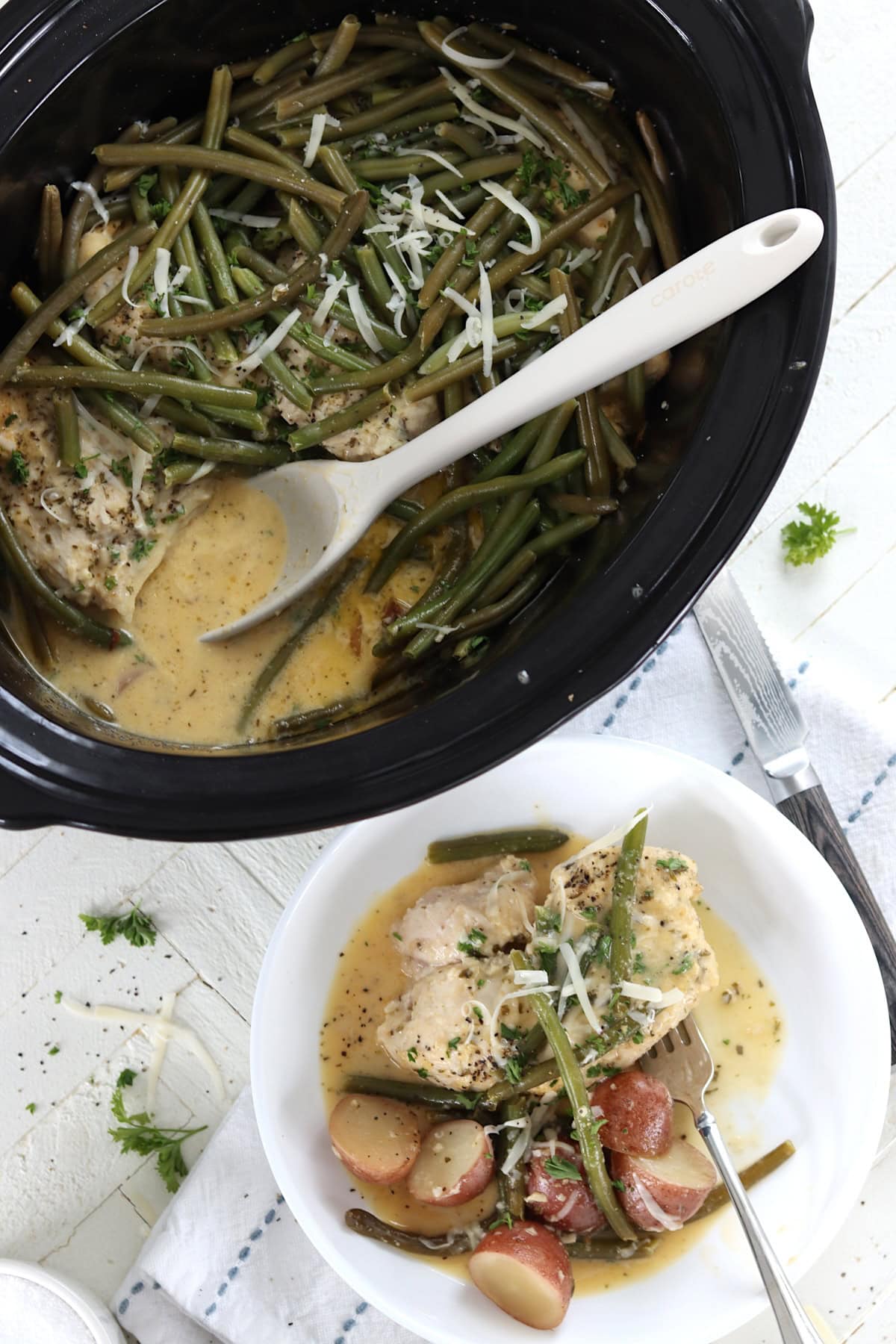 A black crock pot and a white bowl of slow cooker garlic parmesan chicken and potatoes.