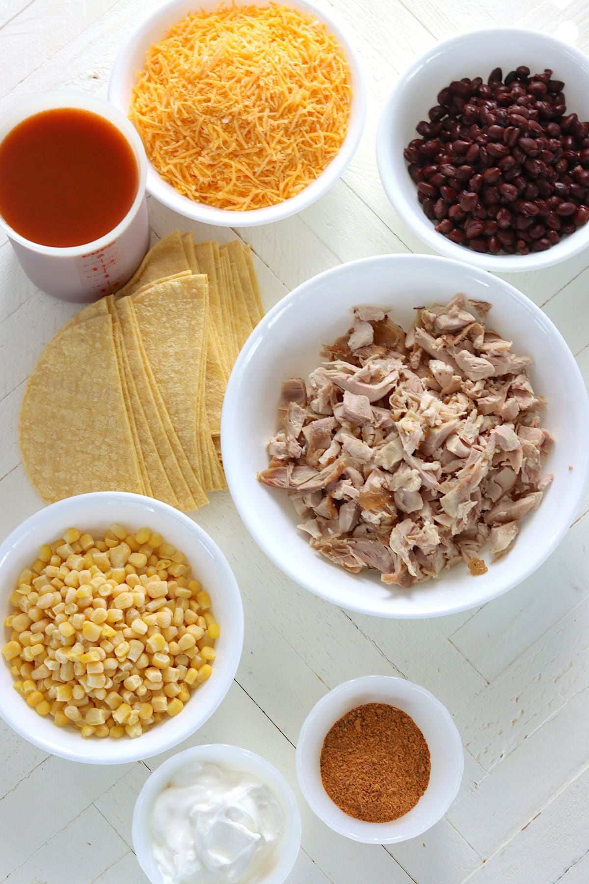 Ingredients needed for making crockpot chicken enchilada casserole on a white wooden board.