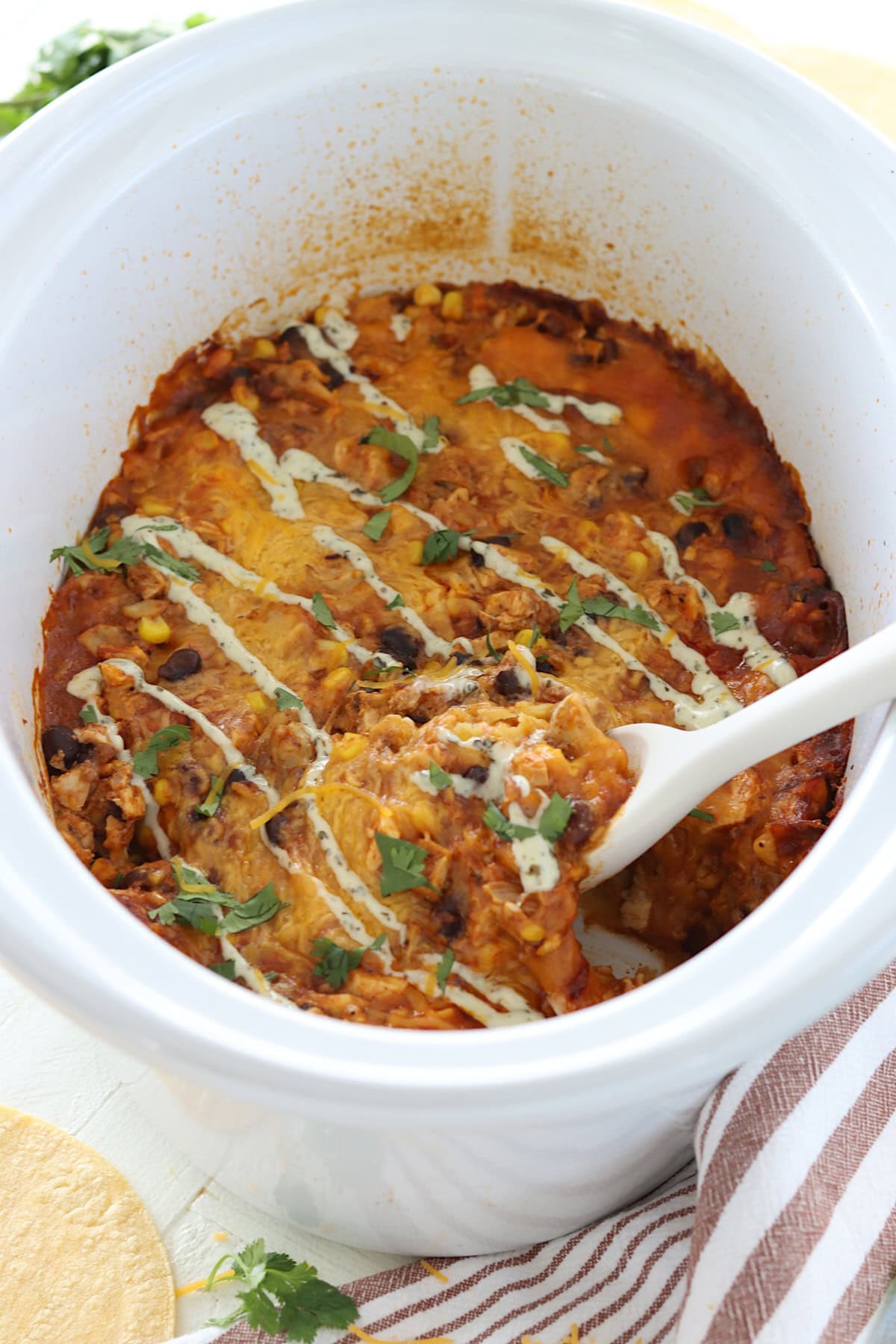 An oval white slow cooker with cooked crockpot chicken enchilada casserole.