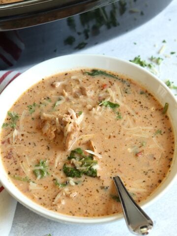 Creamy marry me chicken soup in a white bowl with a spoon and a sprinkle of parmesan cheese.