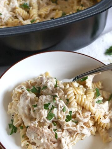 Crockpot garlic parmesan chicken pasta in white bowl and silver spoon.