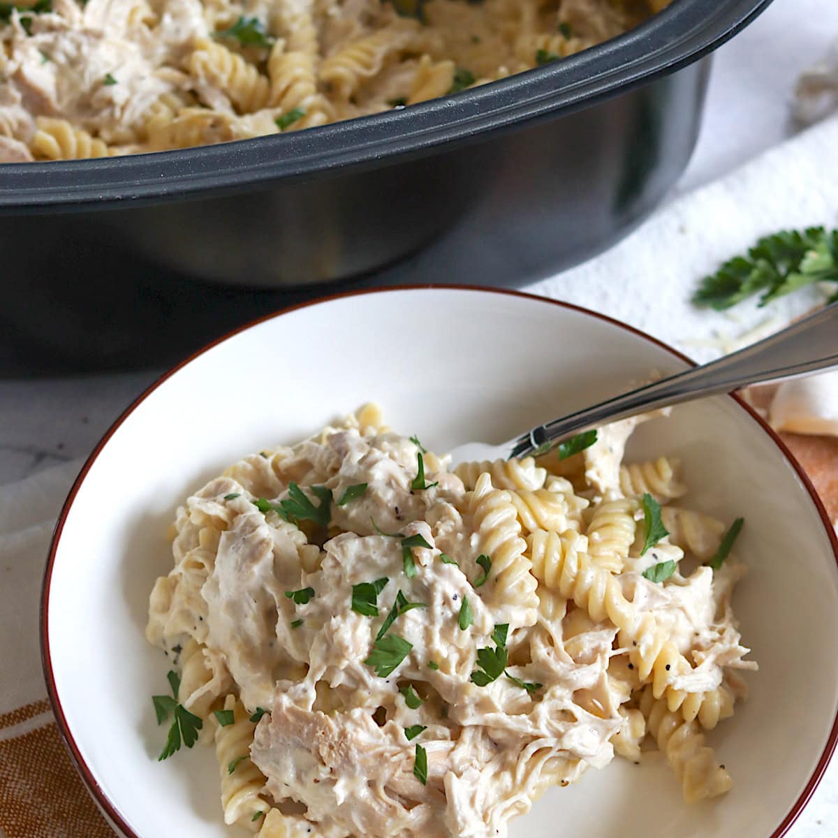 Crockpot garlic parmesan chicken pasta in white bowl and silver spoon.