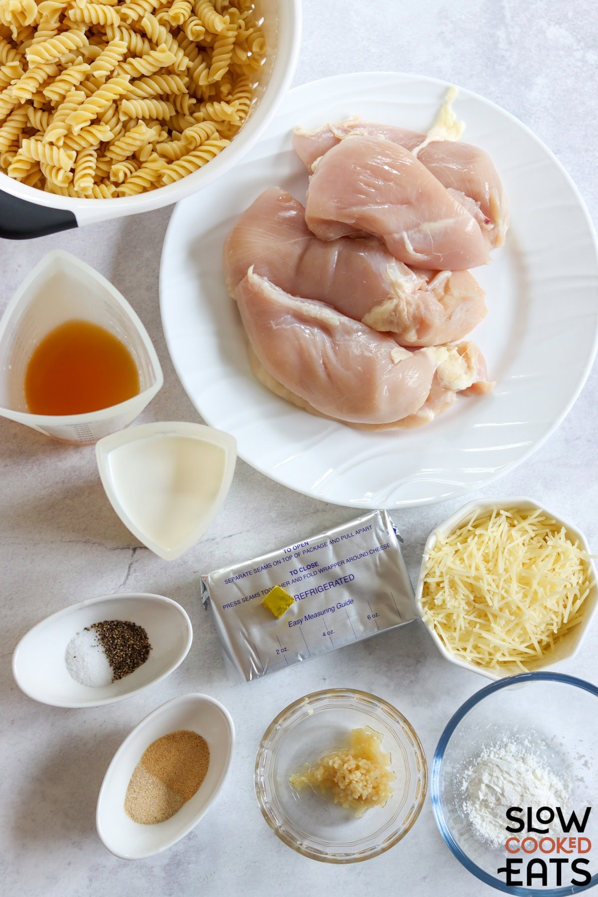 Ingredients needed to make crockpot garlic parmesan chicken pasta on a marble countertop.