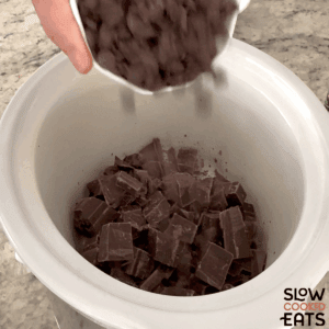 Adding chocolate to a white oval slow cooker for crockpot chocolate candy bar bites.