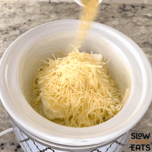 Putting the ingredients to make hot crab dip crockpot recipe into a white oval slow cooker.