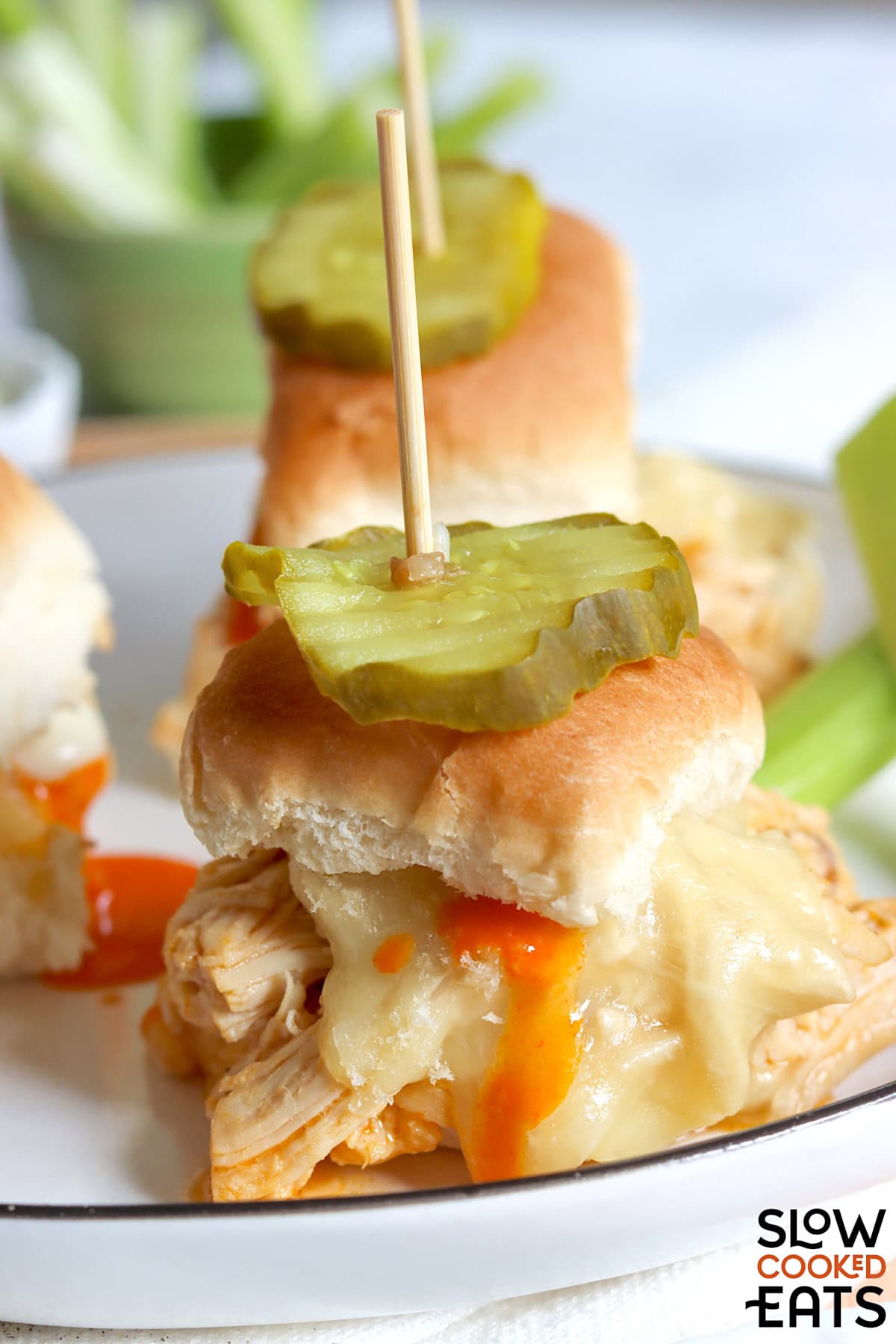 A single crockpot buffalo chicken slider on a white plate topped with a pickle.