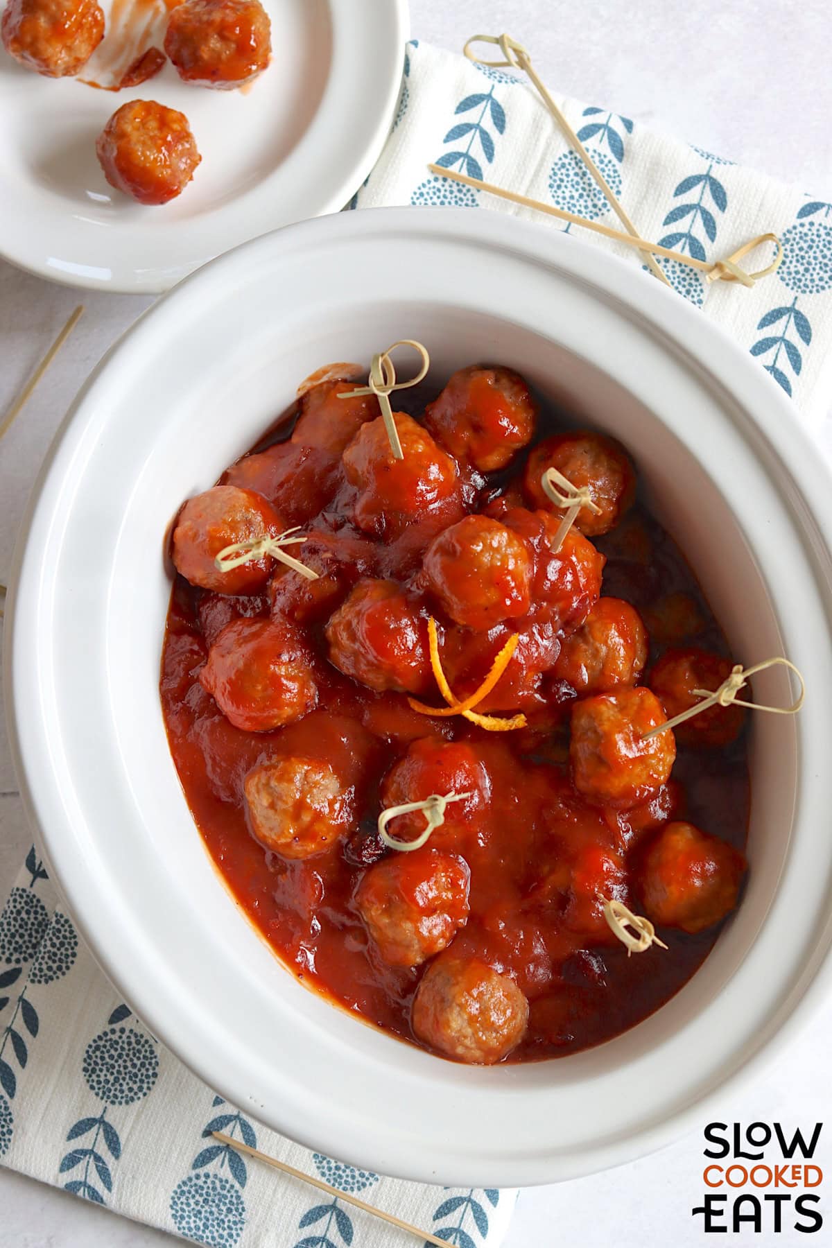 A white oval slow cooker with cranberry meatballs crockpot recipe served with toothpicks.