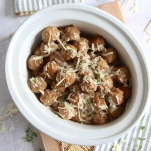 Cheesy French onion soup meatballs crockpot recipe in a white slow cooker on a wooden board with toothpicks for serving.
