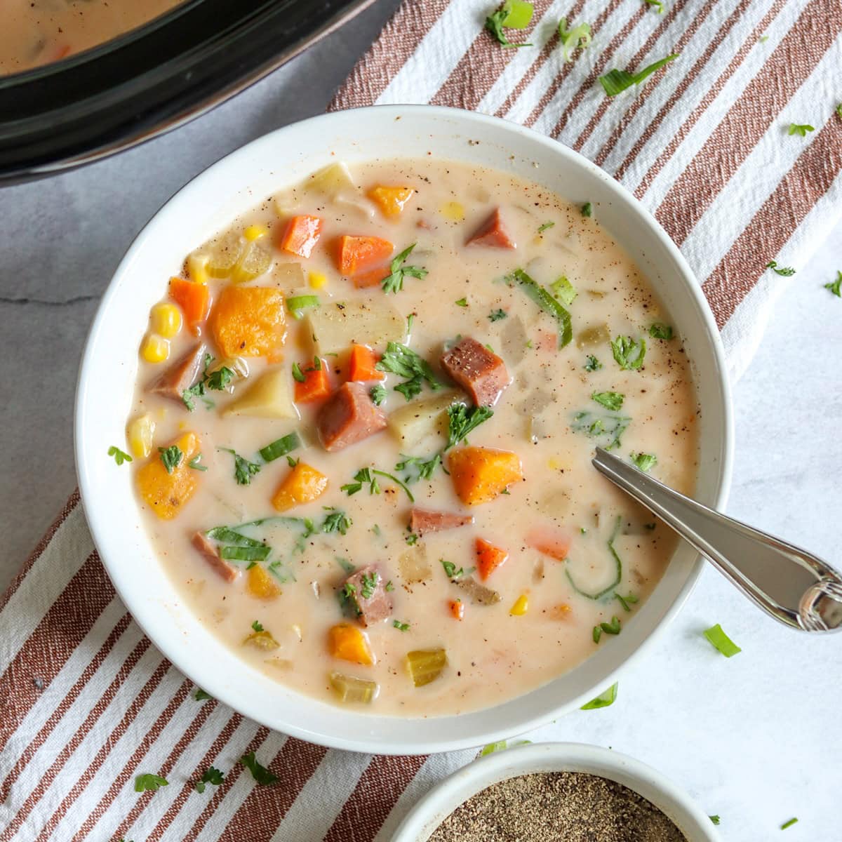 Crockpot ham and potato soup in a white bowl with a spoon.