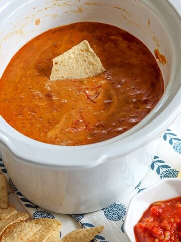 A chip dipped into Hormel chili cheese dip in a white crockpot.