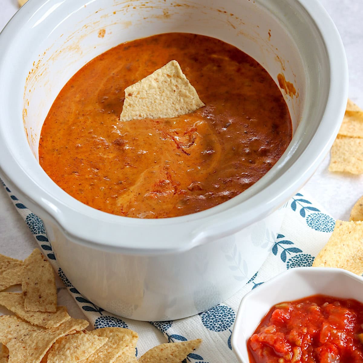 A chip dipped into Hormel chili cheese dip in a white crockpot.