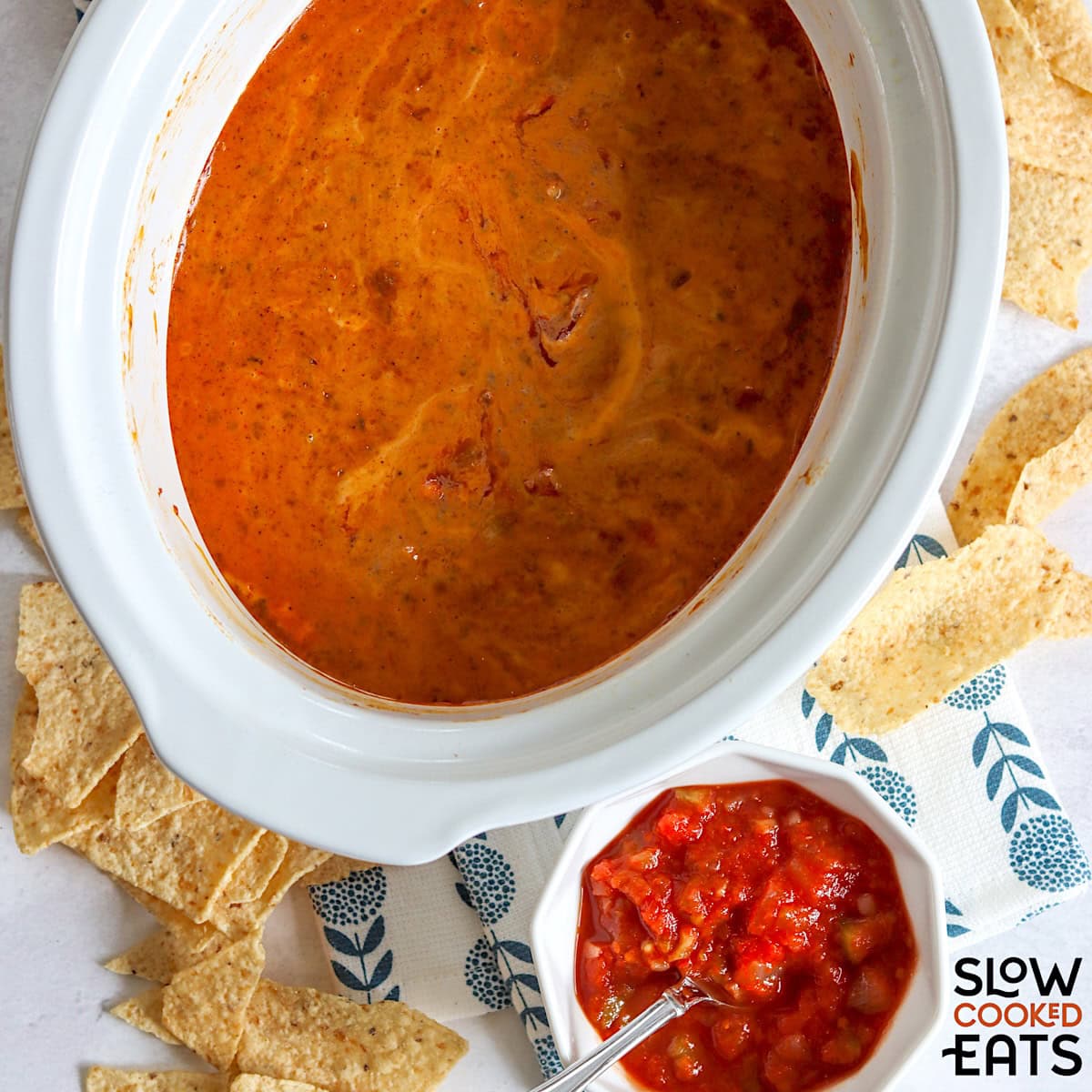 A white oval crockpot of hormel chili cheese dip with salsa.