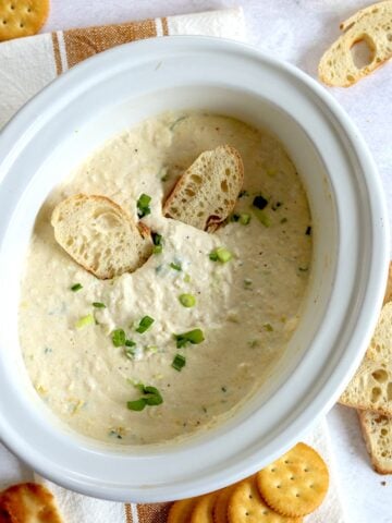 Hot crab dip crockpot recipe in a white oval slow cooker topped with sliced green onion.