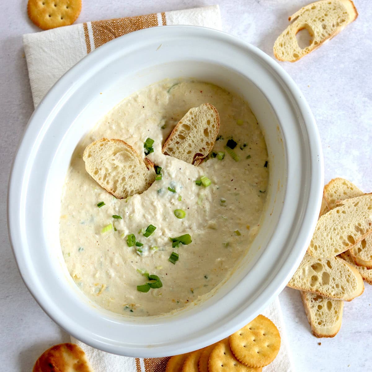Hot crab dip crockpot recipe in a white oval slow cooker topped with sliced green onion.