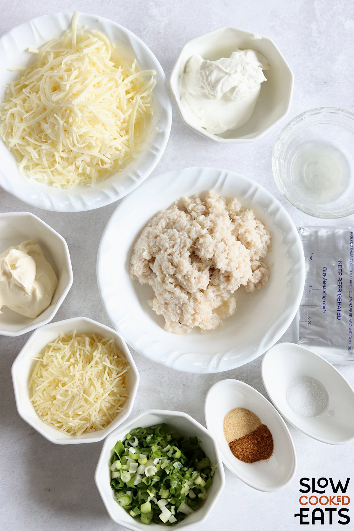 Ingredients needed to make hot crab dip crockpot recipe on a white marble countertop.