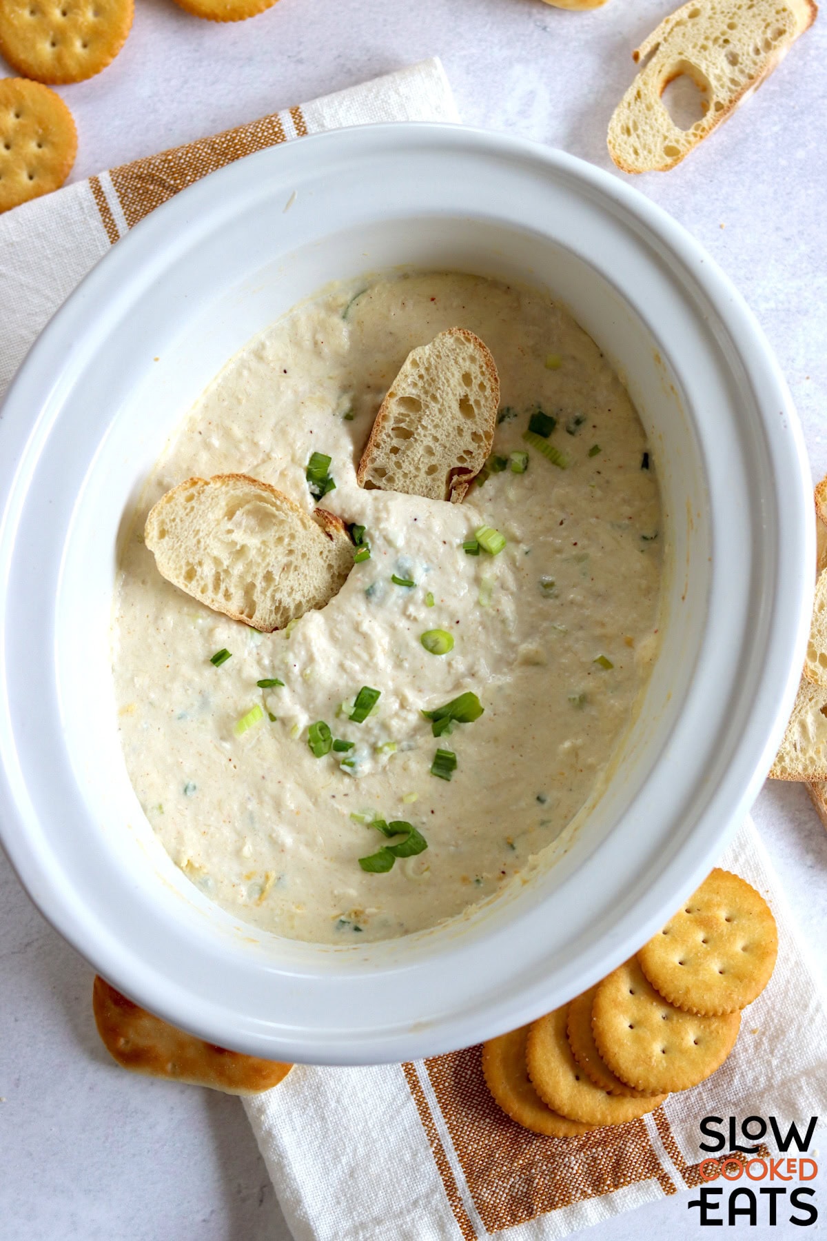 A white oval slow cooker holding hot crab dip crockpot recipe with crackers.