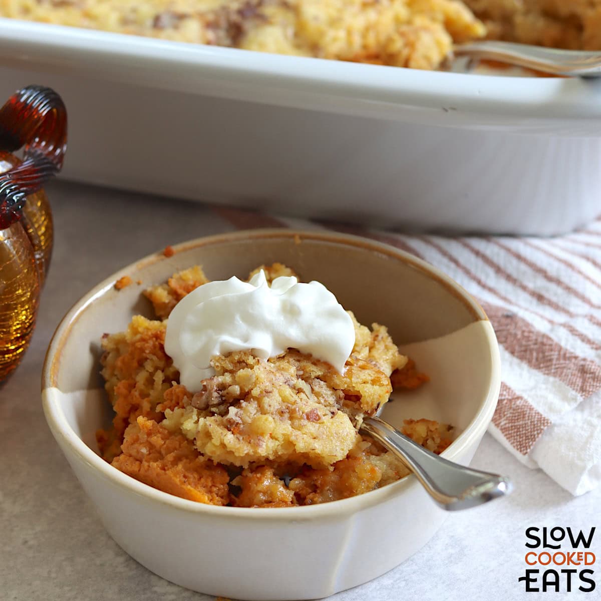 Slow cooker pumpkin dump cake in a small bowl with whipped cream and a spoon.
