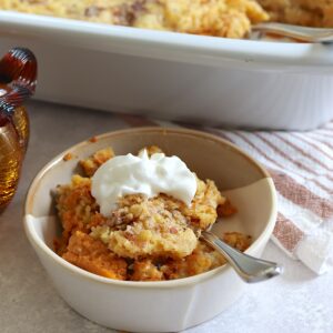 Crockpot pumpkin dump cake served in a small light brown bowl with whipped cream.
