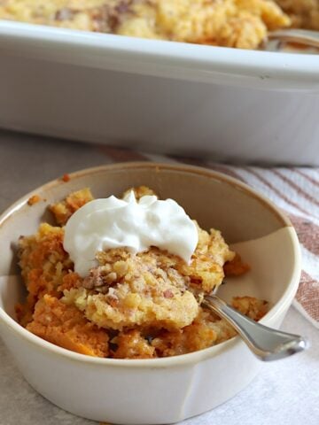 Crockpot pumpkin dump cake served in a small light brown bowl with whipped cream.