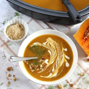 Crockpot butternut squash soup in a white bowl and silver spoon.