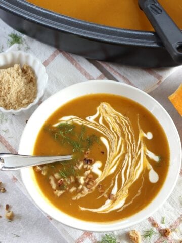 Crockpot butternut squash soup in a white bowl and silver spoon.