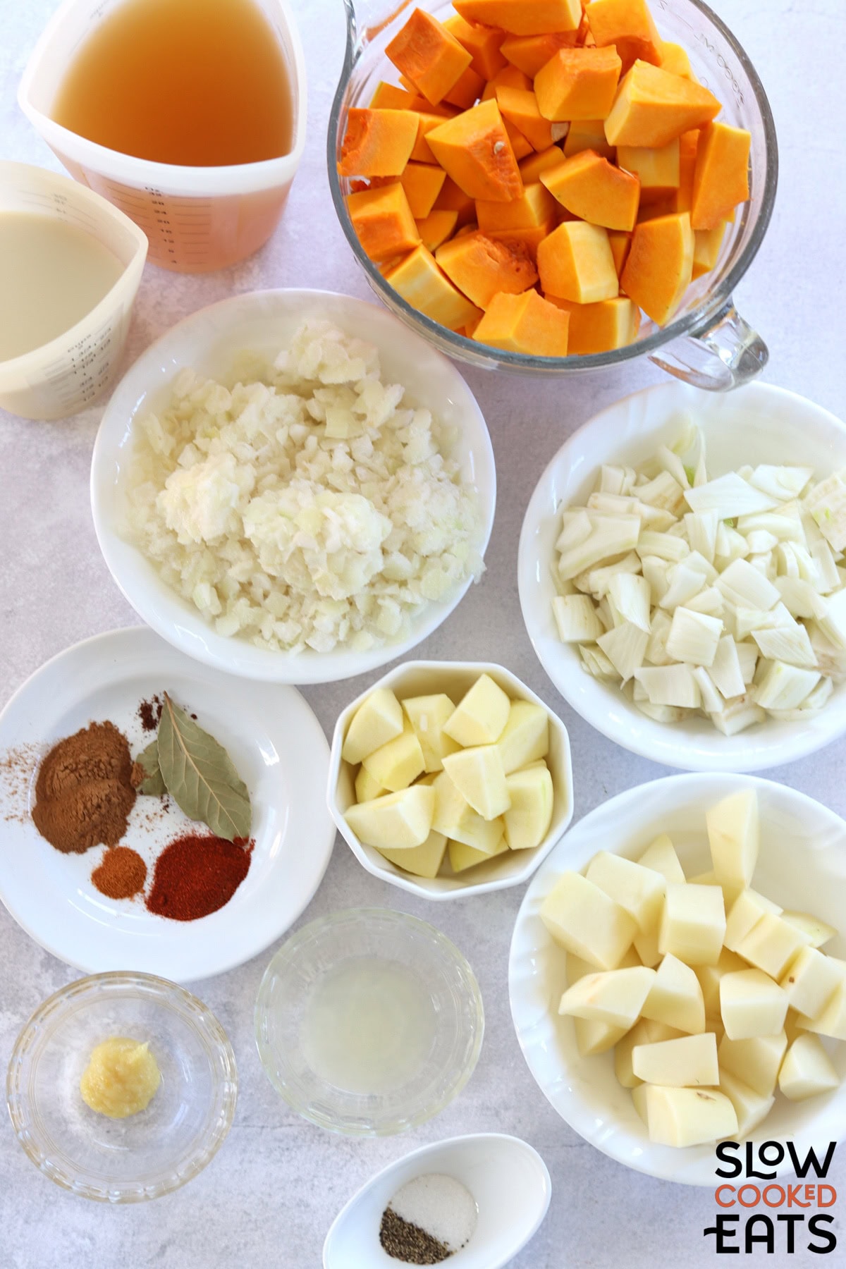 Ingredients needed to make crockpot butternut squash soup on a white marble countertop.