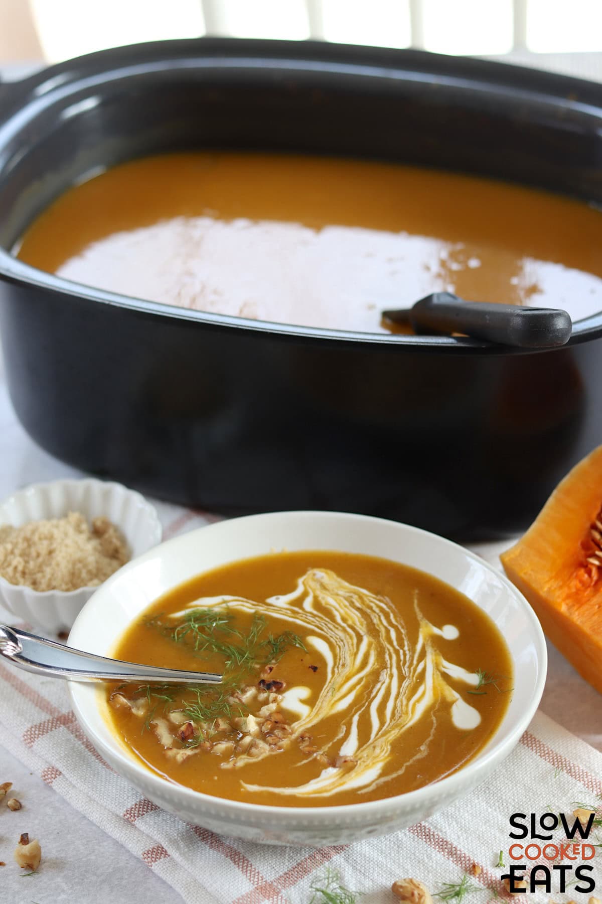 Crockpot butternut squash soup served in a white bowl and silver spoon.