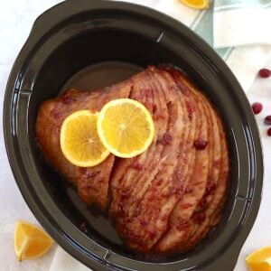Cranberry orange crockpot ham in a black oval slow cooker.