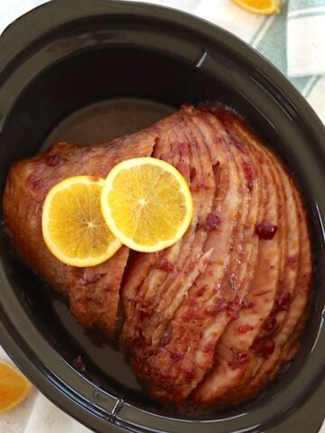 Cranberry orange crockpot ham in a black oval slow cooker.