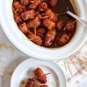 Crockpot little smokies wrapped in bacon in a white oval crockpot.