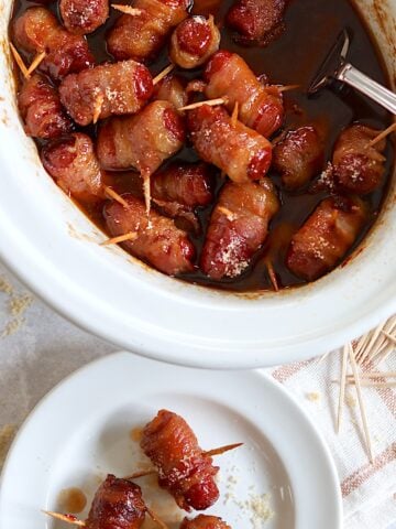 Crockpot little smokies wrapped in bacon in a white oval crockpot.