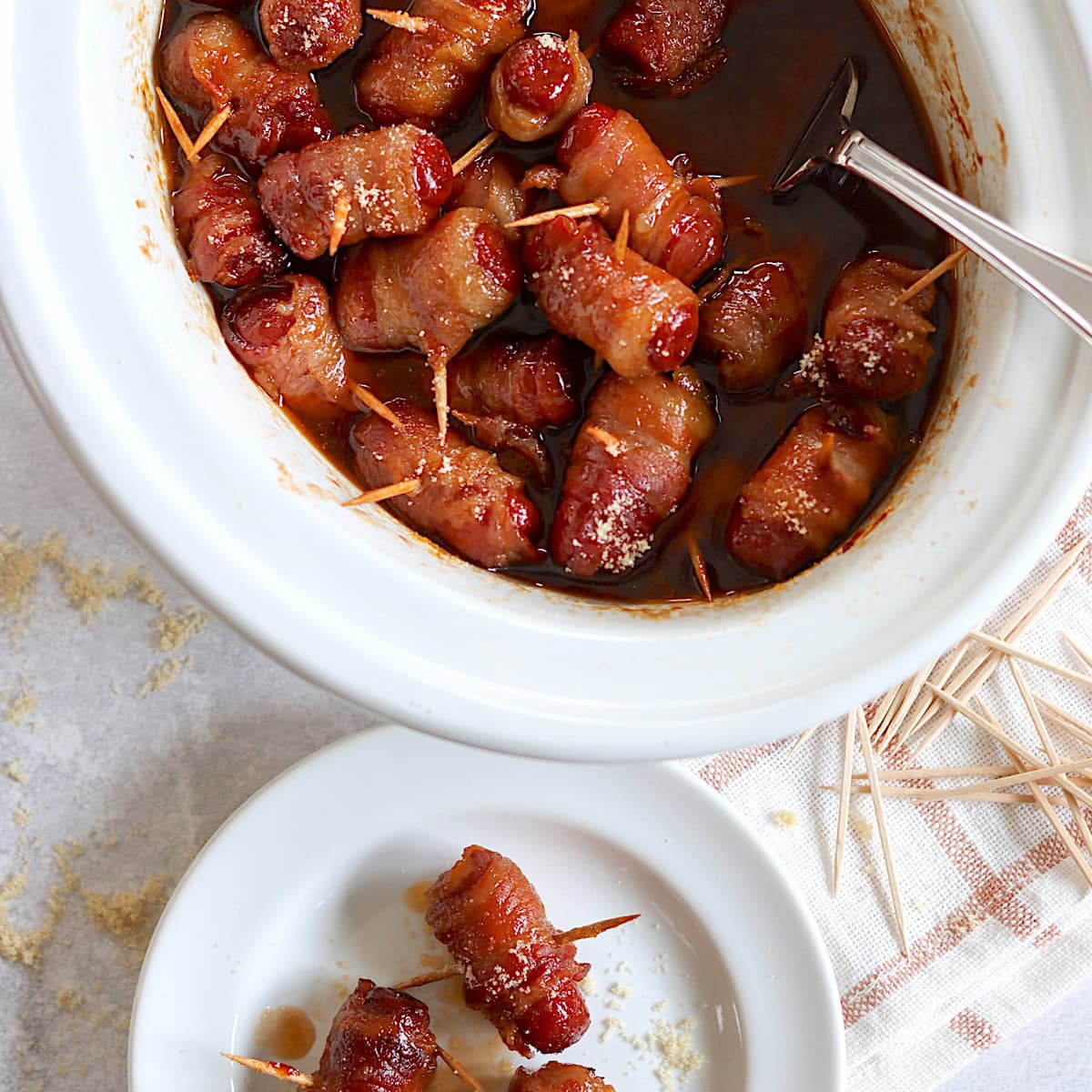 Crockpot little smokies wrapped in bacon in a white oval crockpot.