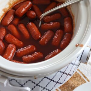 Crockpot little smokies grape jelly in a white slow cooker and silver spoon.
