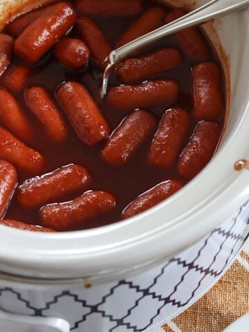 Crockpot little smokies grape jelly in a white slow cooker and silver spoon.