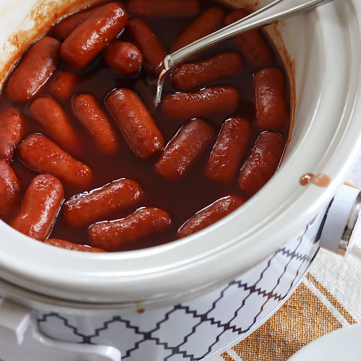 Crockpot little smokies grape jelly in a white slow cooker and silver spoon.