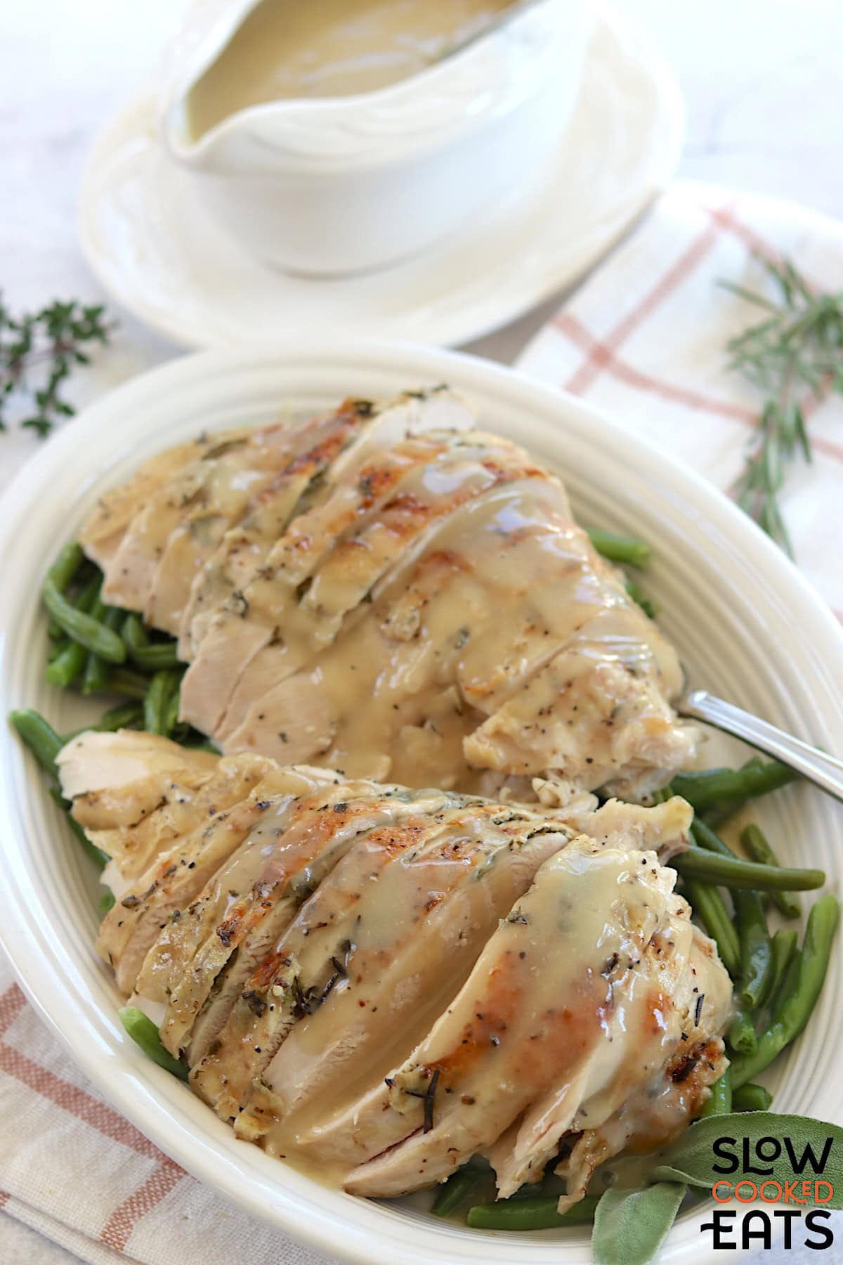 Herb butter slow cooker turkey breast sliced and served on a white plate with green beans.