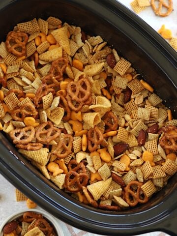 A black oval crockpot filled with parmesan ranch slow cooker Chex mix.
