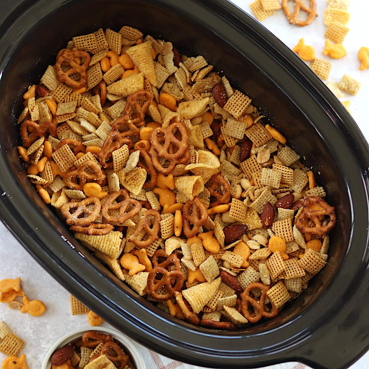 A black oval crockpot filled with parmesan ranch slow cooker Chex mix.