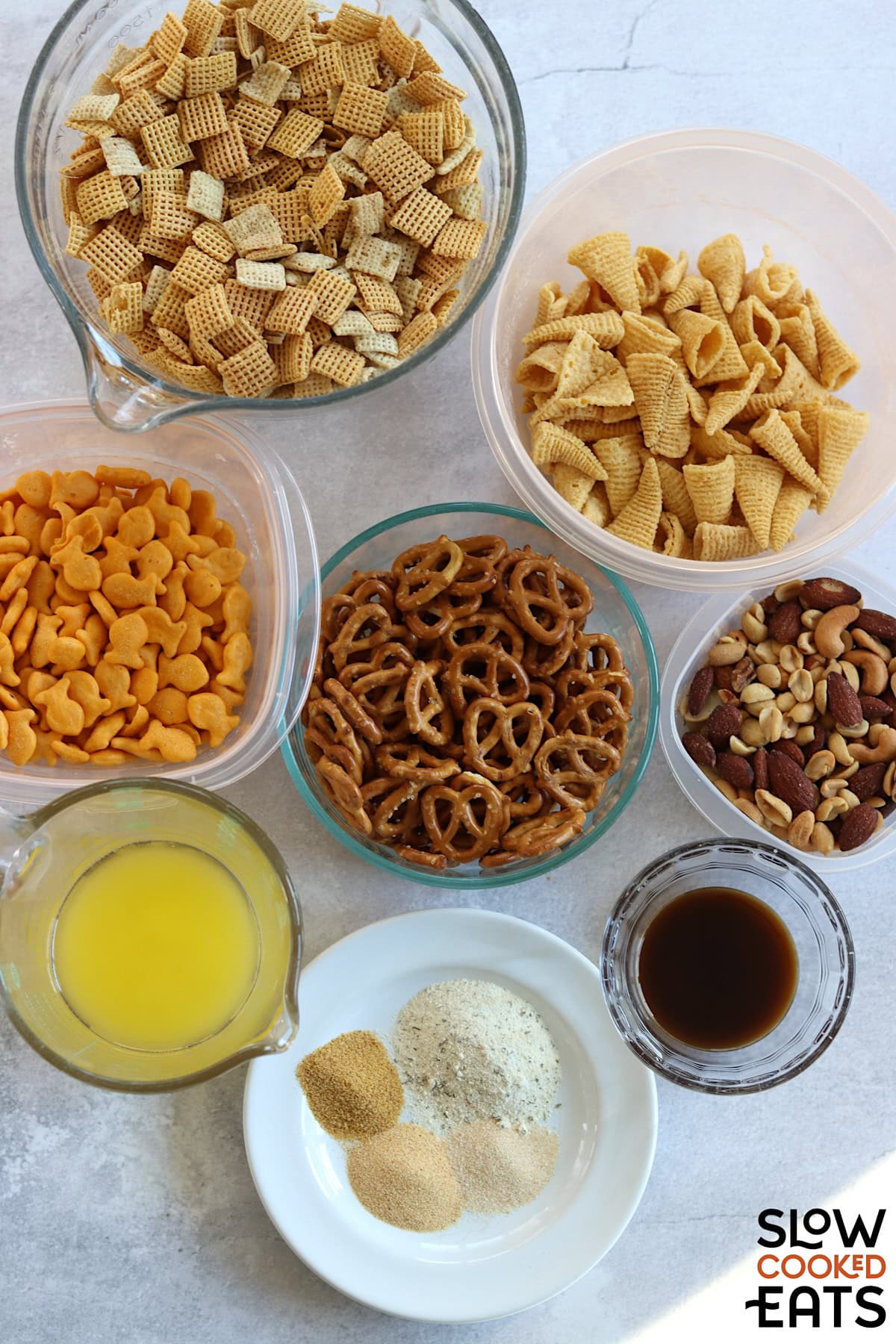 Ingredients needed to make parmesan ranch slow cooker Chex mix on a white marble countertop.