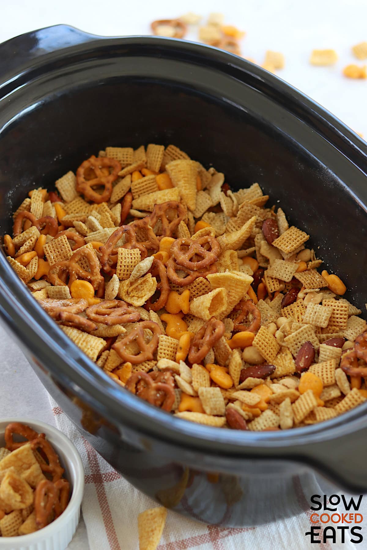 A black oval crockpot filled with parmesan ranch slow cooker Chex mix.