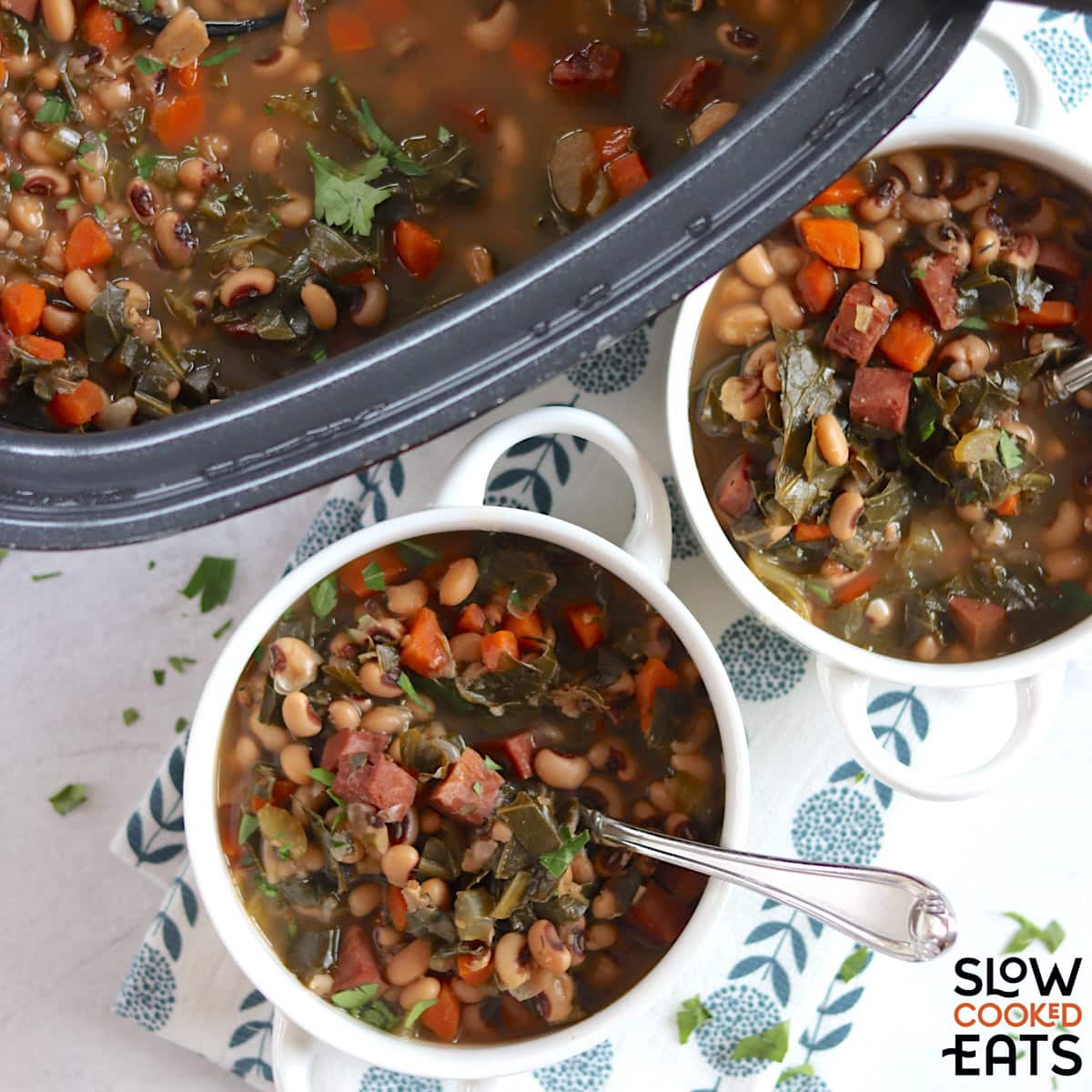 Crockpot Ham and Black Eyed Pea Soup with Collard Greens served in small white crocks and a silver silver spoon.
