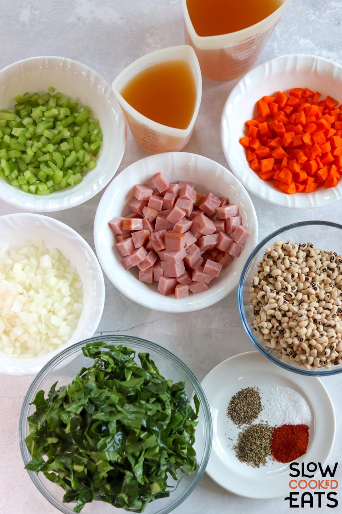 Ingredients needed to make crockpot ham and black eyed pea soup with collard greens on a white marble countertop.