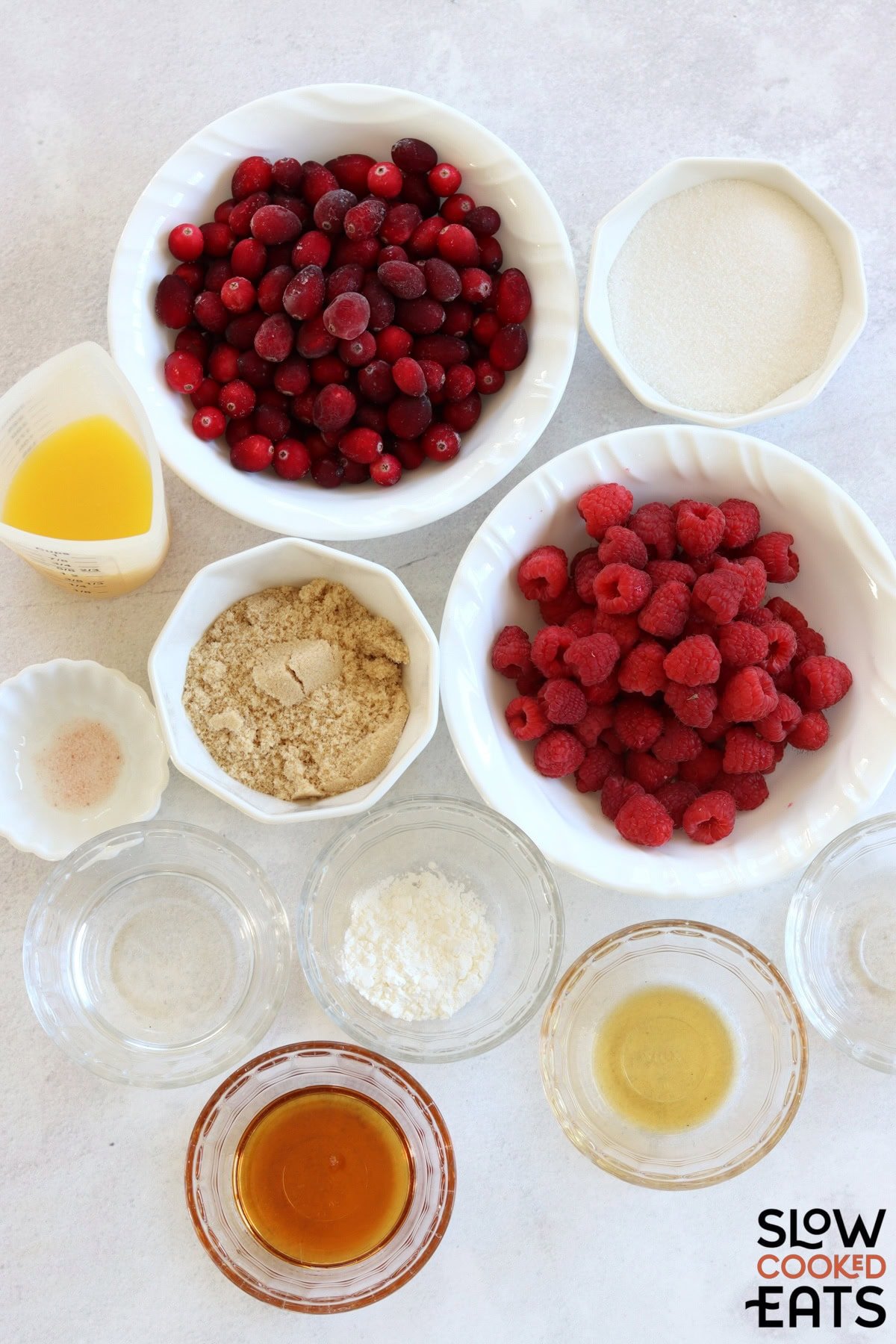 Ingredients needed to make raspberry cranberry sauce crockpot recipe on a white marble countertop.