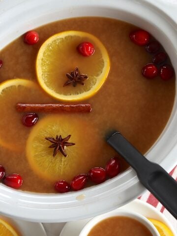 Crockpot Christmas punch in a white oval slow cooker and black ladle.
