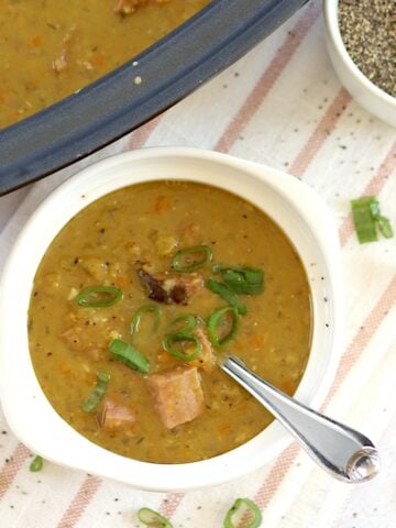 Crockpot split pea and ham soup recipe served in a white round bowl and silver spoon.