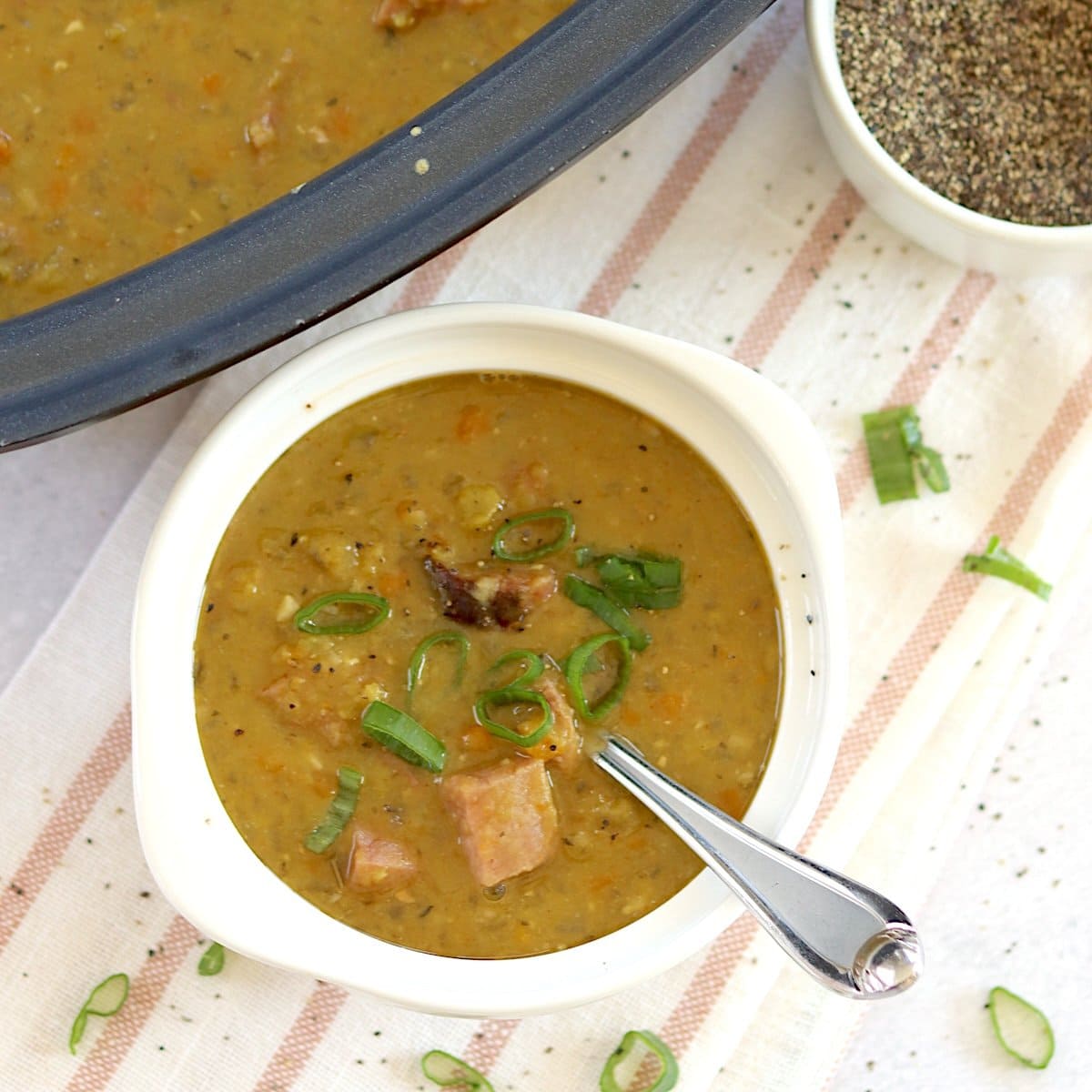 Crockpot split pea and ham soup recipe served in a white round bowl and silver spoon.